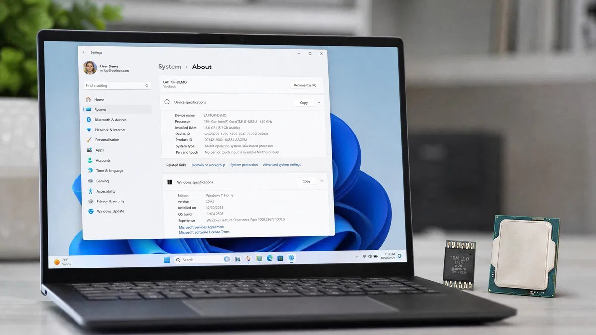Windows 11 requirements: laptop with Settings About page, TPM chip and CPU on the desk